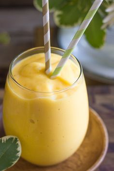 a glass filled with yellow liquid sitting on top of a wooden plate next to a plant