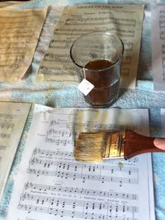 a person holding a paintbrush next to sheet music sheets and a cup of water