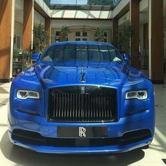 a blue rolls royce parked in front of a large building with a skylight above it