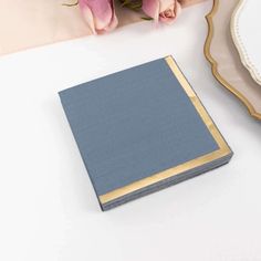 a blue book sitting on top of a table next to pink flowers and a plate