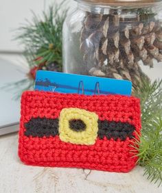 a red crocheted bag with a yellow and black eye on it sitting next to pine cones