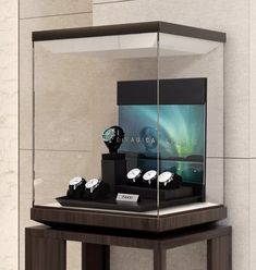 a display case with three watches in it on top of a wooden table next to a wall