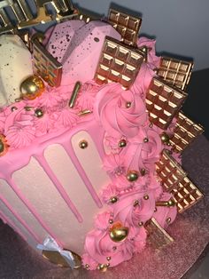 a cake with pink frosting and gold decorations on it's side, sitting on top of a table