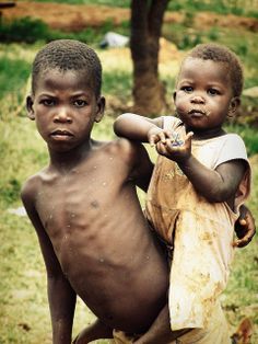 two young boys standing next to each other in front of a tree and grass covered field