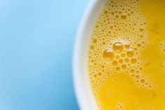 a yellow liquid in a white bowl on a blue background