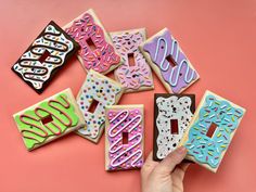 a hand is pointing at decorated cookies on a pink surface with the word boo spelled out