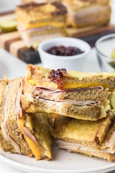 several sandwiches stacked on top of each other with fruit in the background and another sandwich cut in half