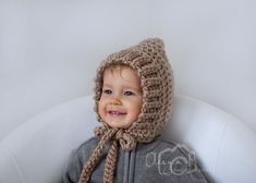 a young child wearing a knitted hat and scarf on top of a white chair