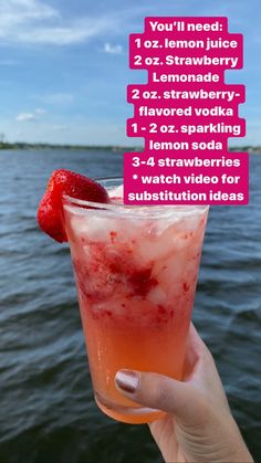 a person holding up a drink with strawberries on it in front of the water