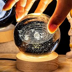 a person touching the inside of a glass ball on a wooden stand with other items around it