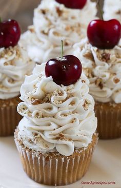 cupcakes with white frosting and cherries on top are sitting on a plate