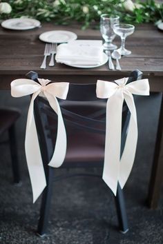 the table is set with plates, silverware and white ribbon tied around the place settings