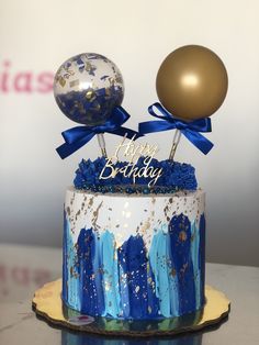 a birthday cake decorated with blue and gold icing, balloons and confetti