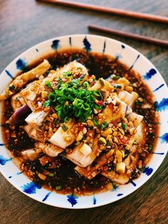 a white and blue bowl filled with food on top of a wooden table next to chopsticks