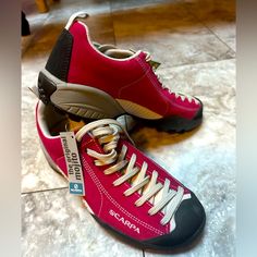 two pairs of red and black shoes sitting on the floor next to each other, one with white laces