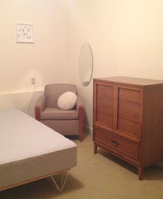 a small bedroom with a bed, chair and dresser in it's corner area