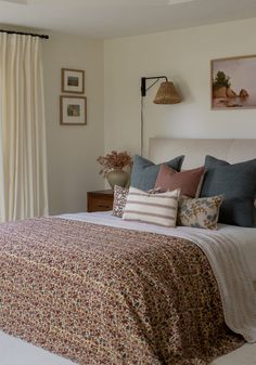 a bed sitting in a bedroom next to a window filled with curtains and pillows on top of it