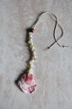 a pink and green necklace on a white surface with a string attached to the bead