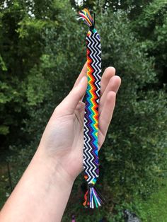 a hand holding a multicolored tie with trees in the background