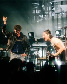 two people standing on stage with microphones in their hands and one person holding his hand up