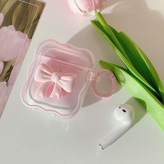 an earbud case with a pink bow on it next to some flowers and a pair of ear buds