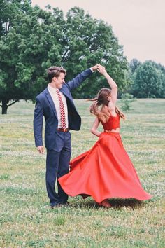 a man in a suit and tie dancing with a woman in a red dress on the grass