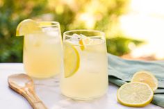 two glasses filled with lemonade sitting on top of a table next to a wooden spoon