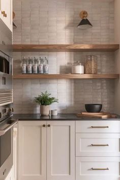 a kitchen with white cabinets and open shelvings on the wall, along with a potted plant