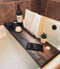 a bottle of wine sitting on top of a bath tub next to an open book