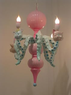 a pink chandelier with two cats hanging from it's sides and three candles in the middle