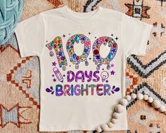 a t - shirt with the words 100 days brighter on it next to beads and other items