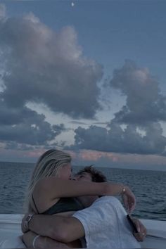 two people embracing each other on a boat in the ocean at dusk with clouds overhead