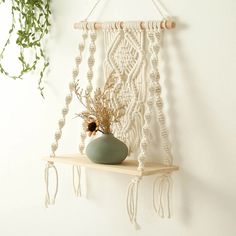 a white macrame hanging on a wall with a vase and plant in it