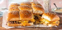 two cheeseburger sandwiches cut in half on top of a cutting board with other food items