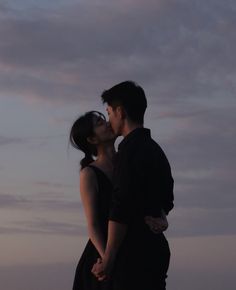 a man and woman kissing in front of the sky at sunset or dawn with their arms around each other