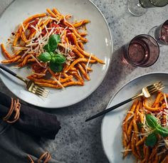 two plates of pasta with cheese and basil on the side, next to wine glasses