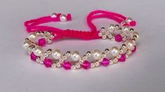 a pink string bracelet with pearls and beads on it, sitting on a white surface