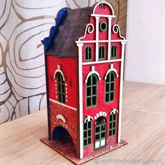 a red and white doll house sitting on top of a wooden table next to a wall