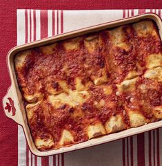 a casserole dish with cheese and sauce in it on a red and white towel