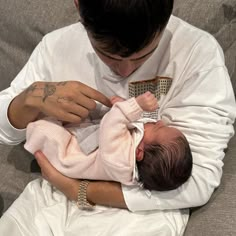 a man holding a baby in his arms while wearing a white shirt and bracelets