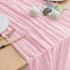 the table is set with plates, silverware and flowers on top of pink cloth