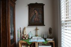 an open book on a table in front of a window with a painting above it