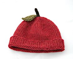 a red knitted hat with a green leaf on it's tip, against a white background