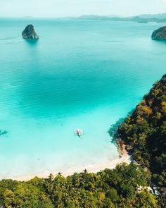 an aerial view of two boats in the water near some mountains and trees on the beach