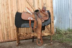 a brown and black horse saddle sitting on top of a wooden stand next to a fence