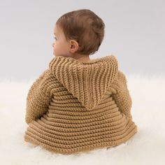 a baby wrapped in a sweater sitting on top of a white rug