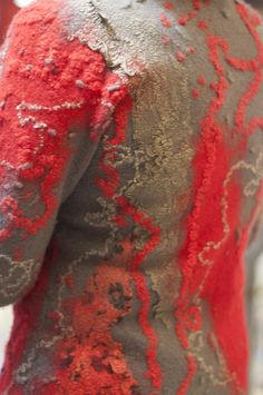 the back of a man's shirt covered in red and grey paint, with his hands on his hips