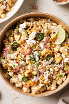 a bowl filled with mexican corn salad next to two bowls full of other food items