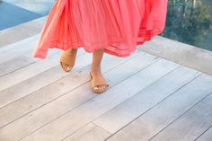 a woman in an orange dress is walking on a wooden deck near a pool and water