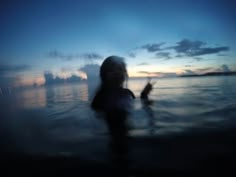 a blurry image of a person standing in the water at sunset or dawn,